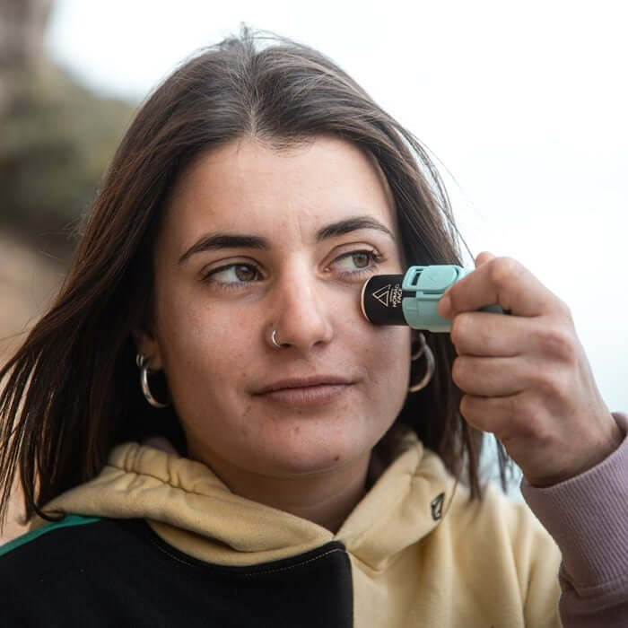 Mujer aplicando protector solar Nomad Face Stick SPF50 en su rostro al aire libre.